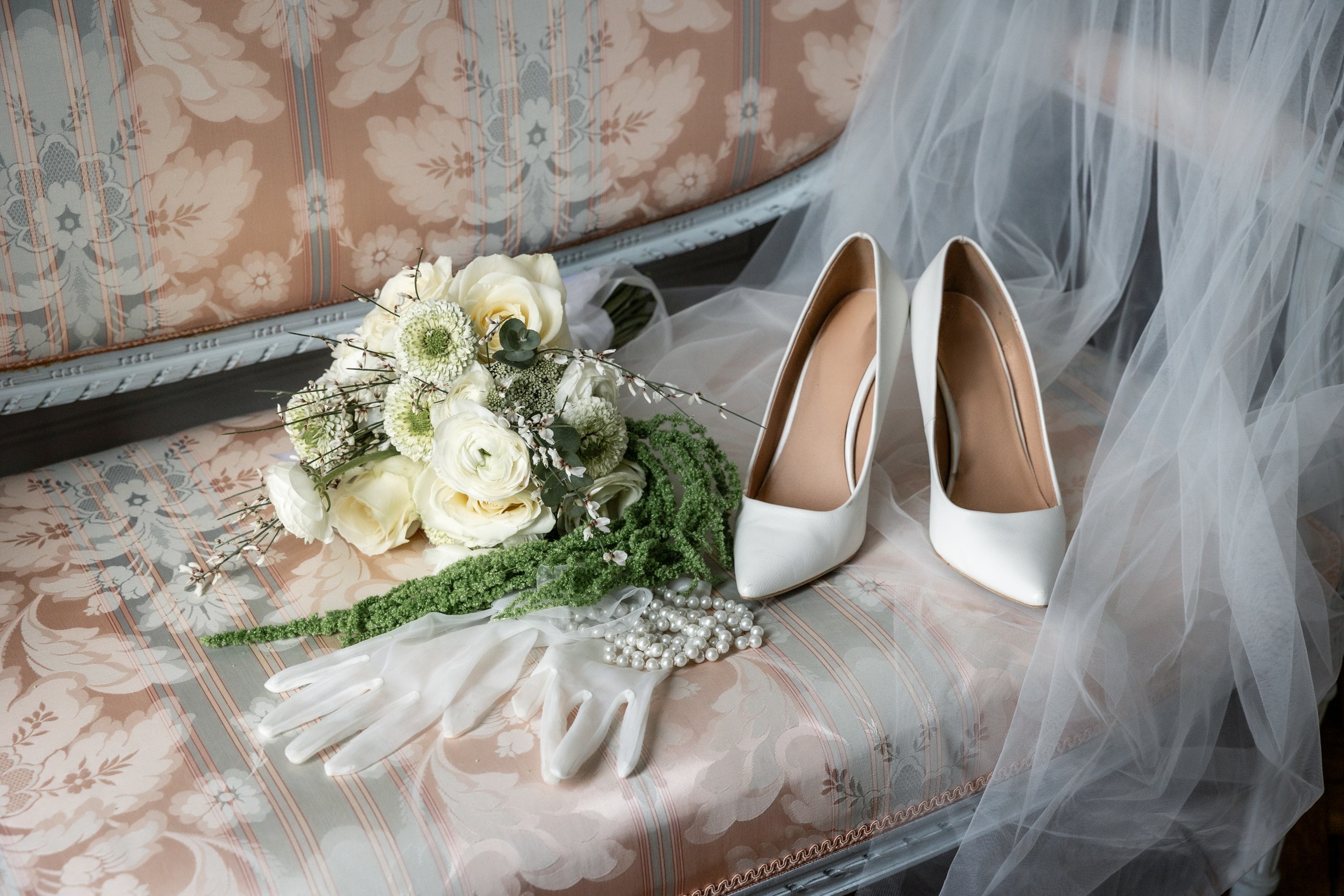 A white rose bridal bouquet, veil and shoes laid out on a period settee at Château de Bonnemare