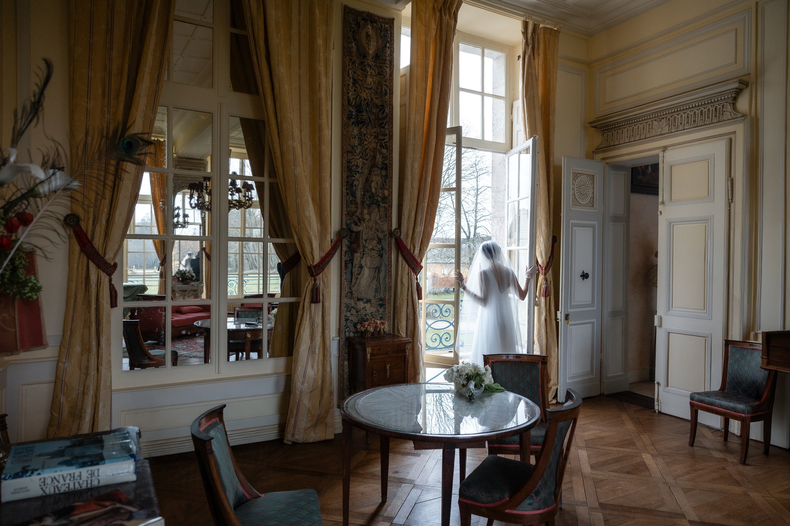 The bride at a tall window overlooking the grounds of Château de Bonnemare